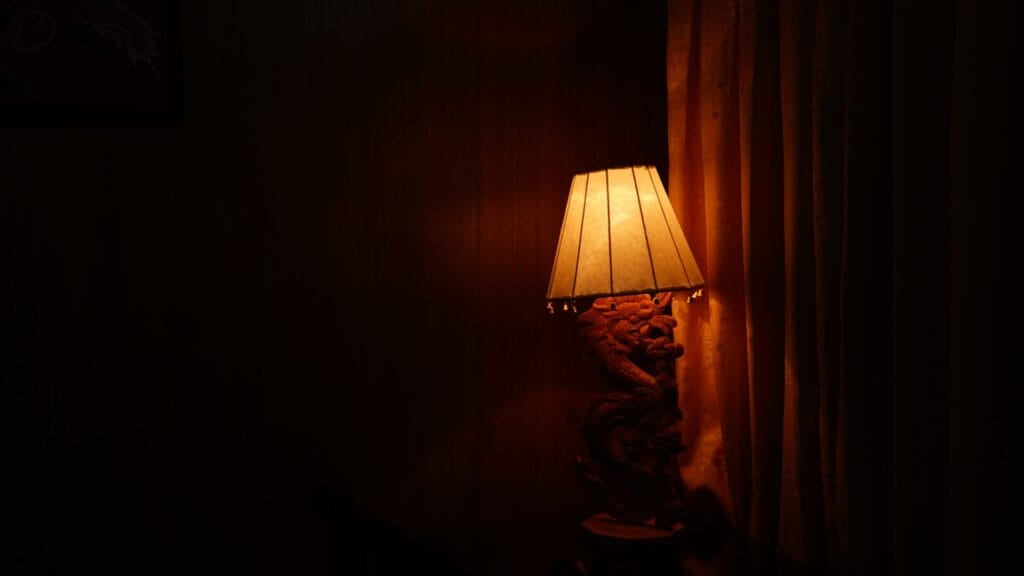 A Dimly Lit Room With A Decorative Lamp On The Right, Casting A Warm Glow On The Curtain Beside It.