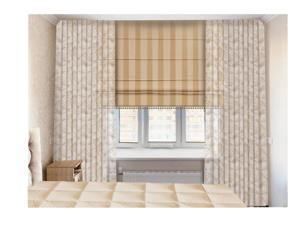 A bedroom window with striped Roman shades and floral-patterned curtains. A beige quilted bedspread is visible in the foreground.